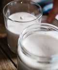 White oat milk in a glass jar and a drinking glass, resting on a wooden table.