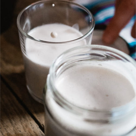 White oat milk in a glass jar and a drinking glass, resting on a wooden table.